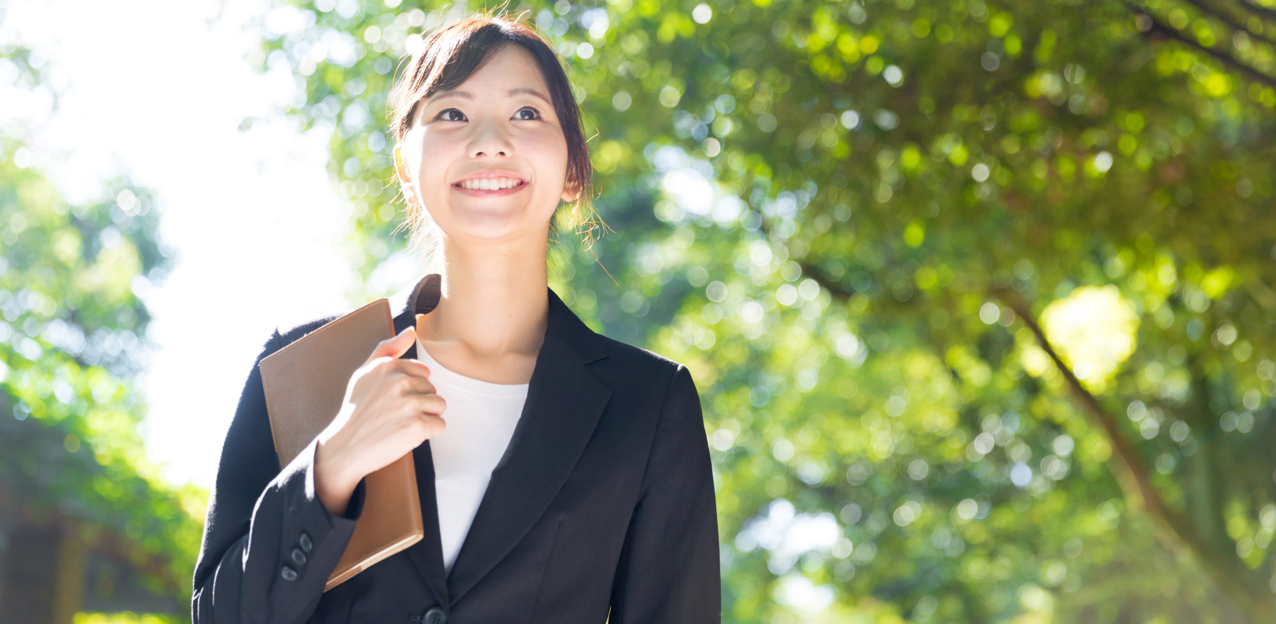 Groupe Y Nexia prime exceptionnelle de pouvoir d’achat, femme souriante en extérieur tenant un carnet contre elle.